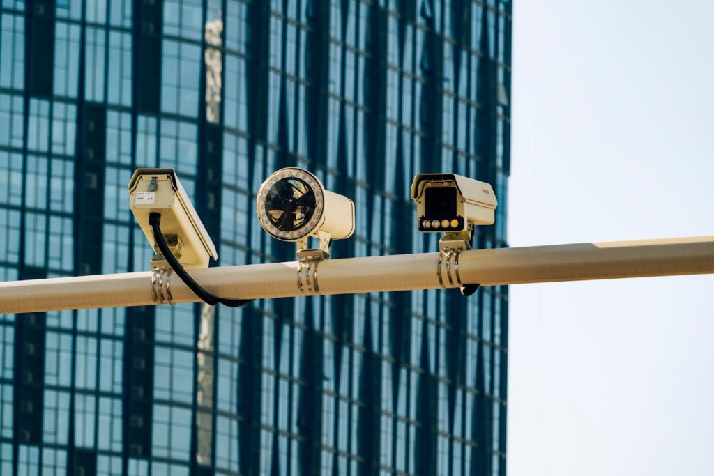 pexels photo 19782580 Surveillance cameras mounted on a pole in front of a modern glass building.